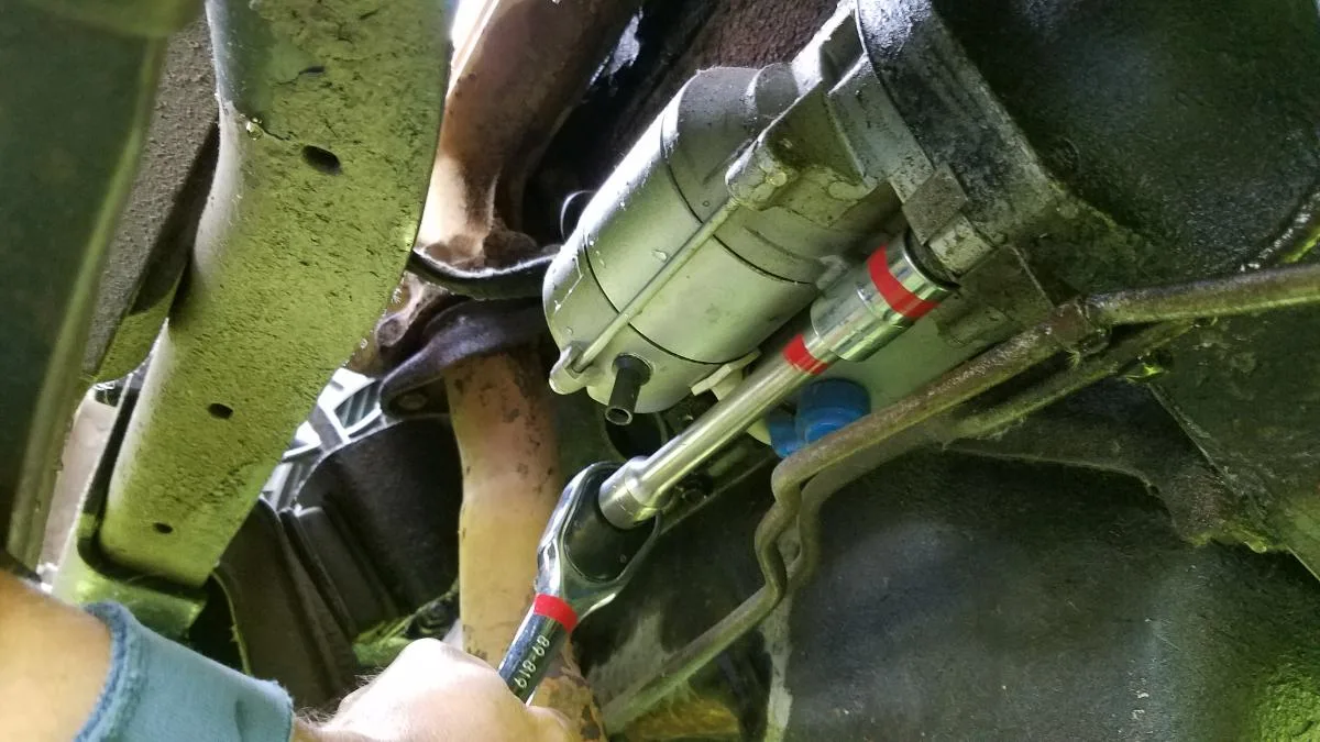 mechanic replacing starter under car